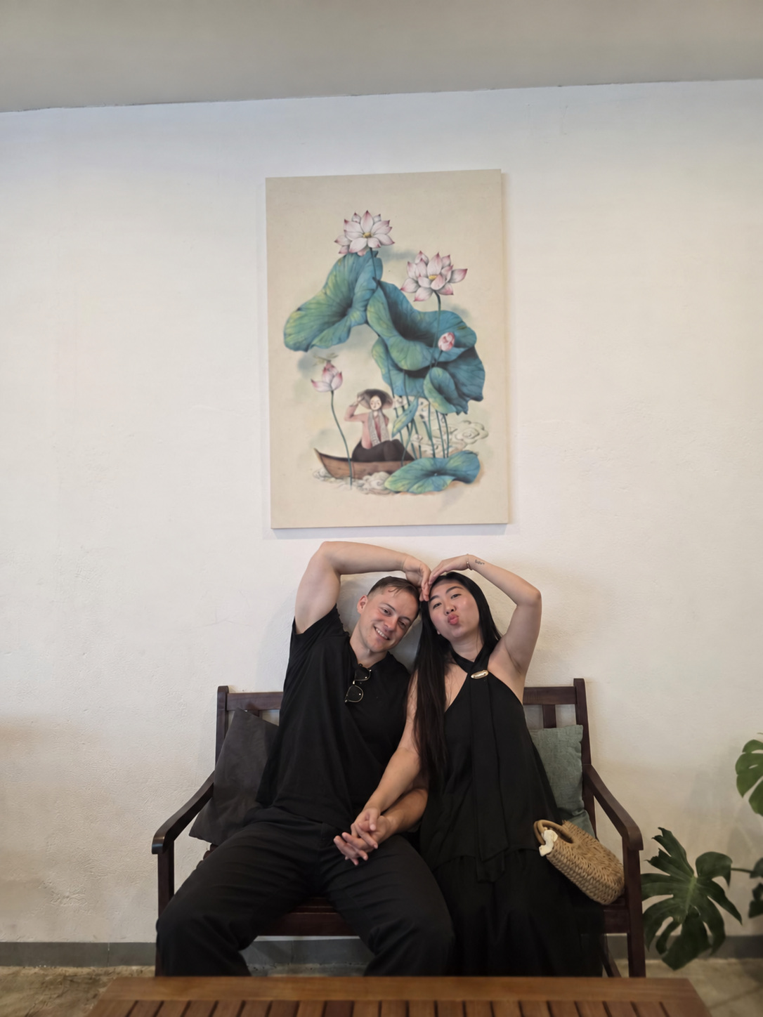 Zach and Xuan holding hands and making a heart with their arms, beneath their lotus artwork